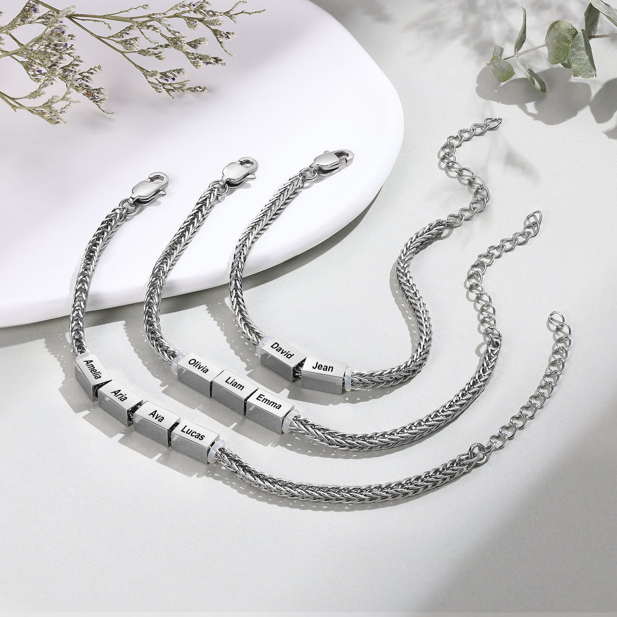 Four silver wheat-chain family bracelets with two to four engraved name charms laid out together